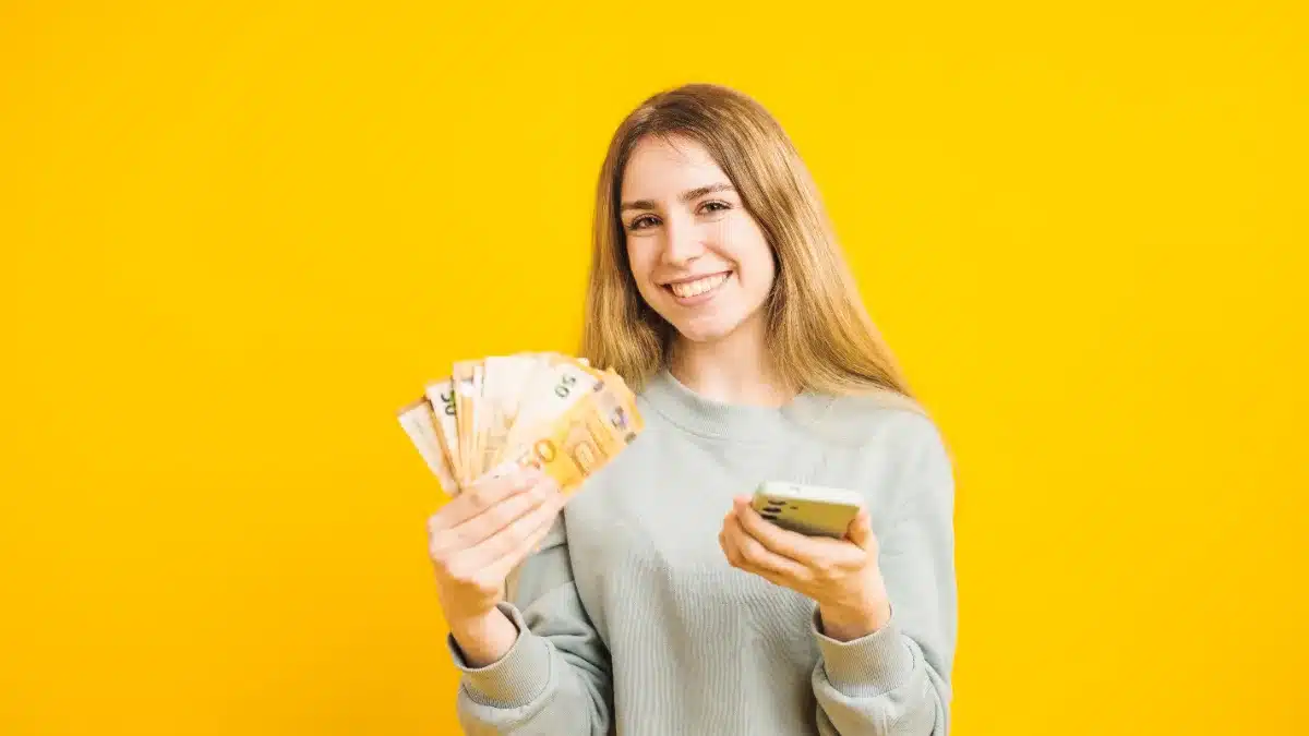 Tânără zâmbind cu bancnote euro și smartphone, ilustrând veniturile din videochat