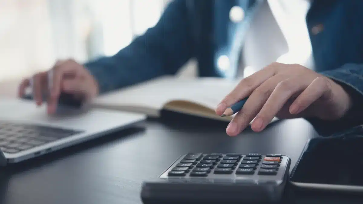 Tânără calculând bugetul lunar și câștigurile din videochat cu un calculator de birou