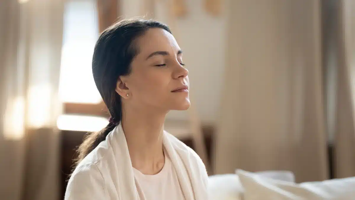 Tânără cu ochii închiși, respirând calm acasă, exercițiu de liniștire înainte de a porni camera