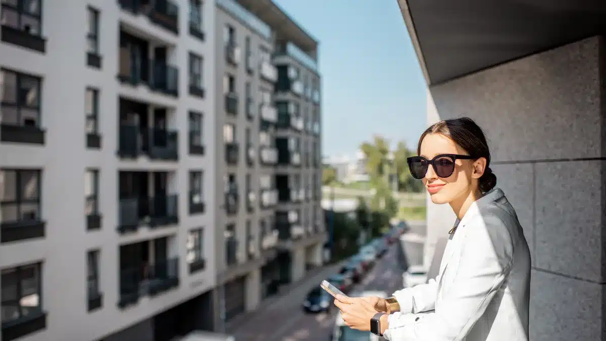 Tânără pe balconul unui apartament, privind un cartier rezidențial modern — alegerea orașului potrivit pentru un studio de videochat